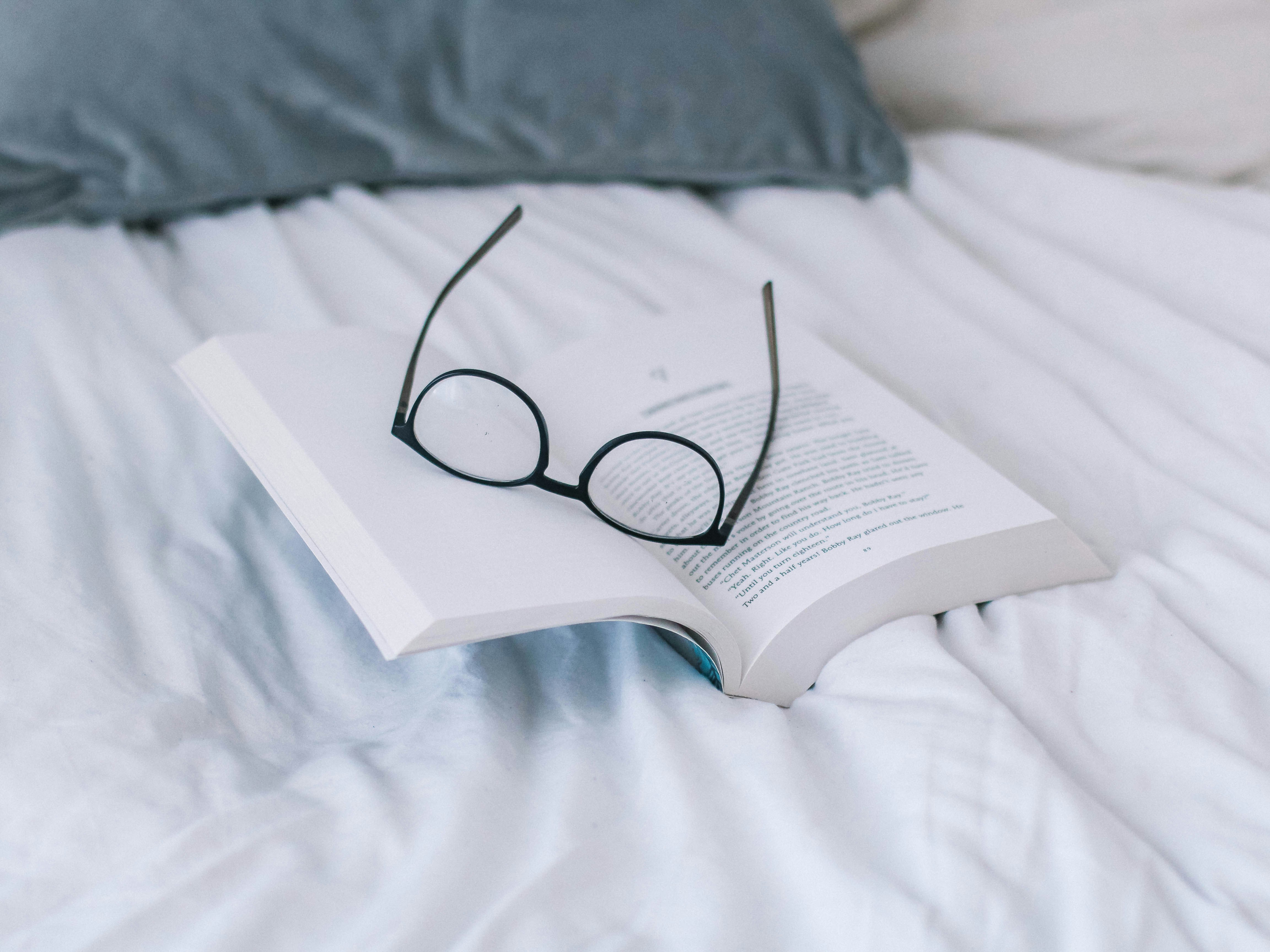 book and round black glasses on white sheets