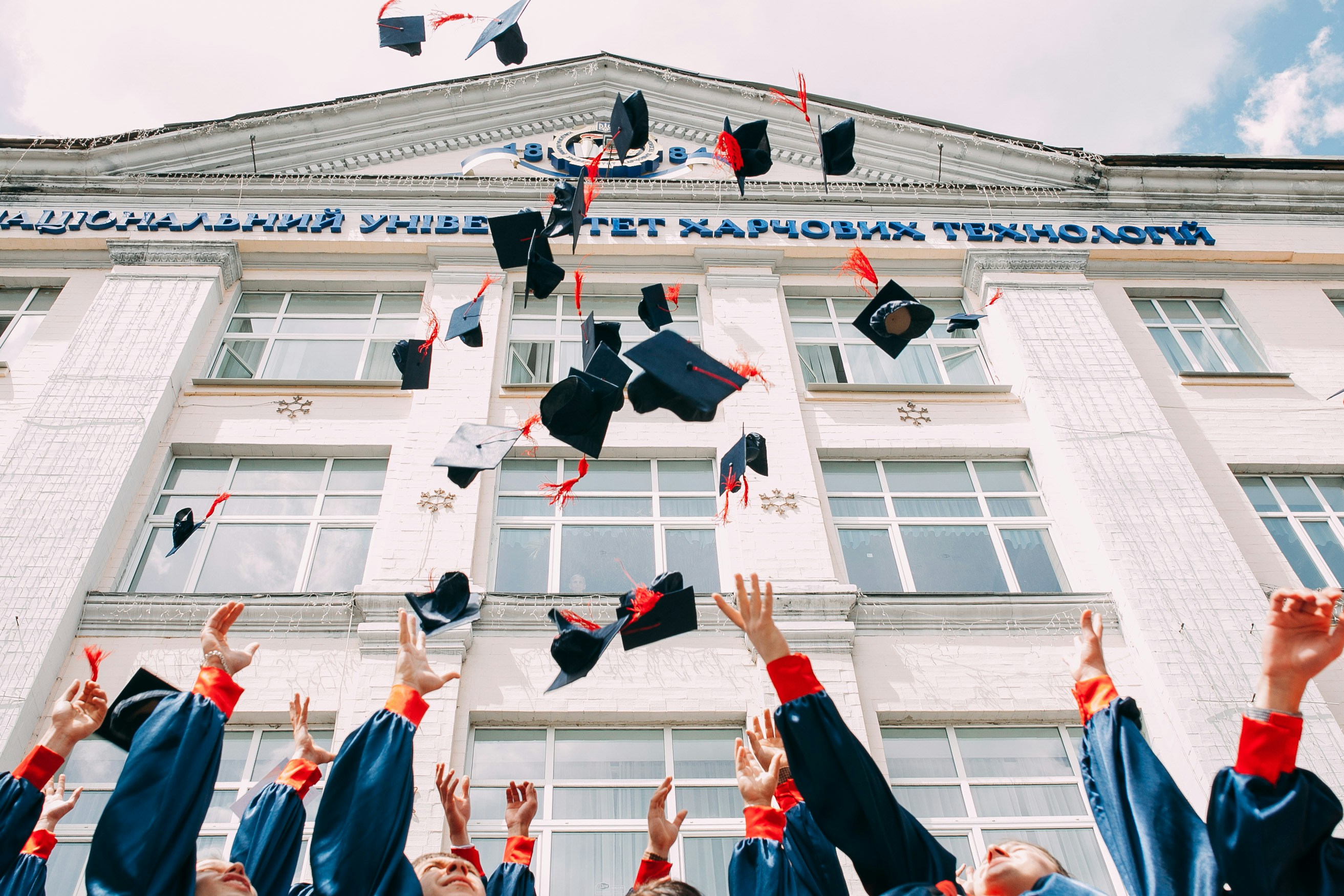 college students throwing grad caps in front of white building